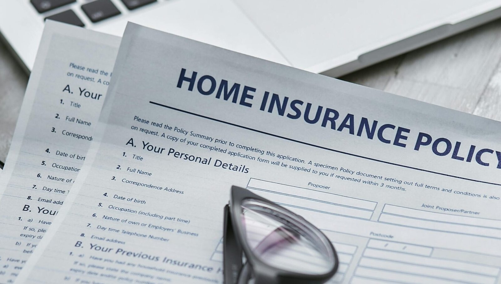 Close-up of home insurance policy document with glasses and laptop on a table.
